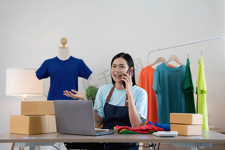 确认订单摄影照片_美丽的亚洲女性在线卖家通过电话确认客户的订单，创办小型企业的中小企业主女企业家在家里使用笔记本电脑、包装和交付情况概念。