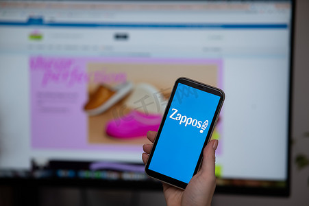 2022 年 12 月 3 日哈萨克斯坦阿拉木图：不露面的女人拿着智能手机，显示器背景上有 Zappos 标志。