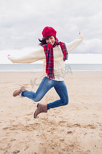 穿着时尚保暖衣服的女人在海滩上跳跃