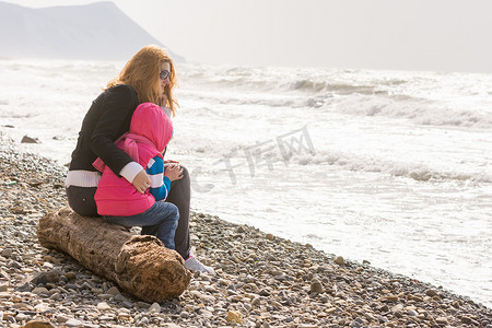 我妈妈和五岁的女儿坐在沙滩上，妈妈抱着她冻僵的女儿