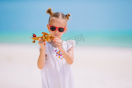 快乐的小女孩在沙滩上玩玩具飞机。