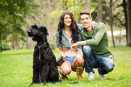 雪纳瑞摄影照片_年轻夫妇与黑色巨型雪纳瑞犬