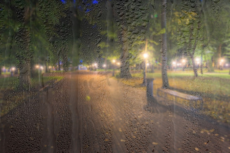 在雨天、湿漉漉的后面，灯笼和长椅散焦的夜间公园