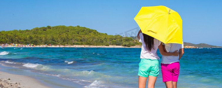 带黄色雨伞的白色沙滩上浪漫情侣的背影