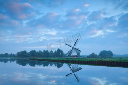 在平静的日出期间靠近河流的荷兰风车