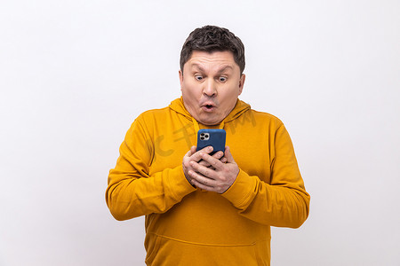沉迷手机摄影照片_惊讶的中年男子使用手机，表情震惊，沉迷于智能手机。