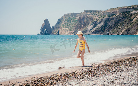 可爱的小女孩在清澈湛蓝的大海的映衬下沿着海边奔跑，在夏日的阳光下欢欣鼓舞。