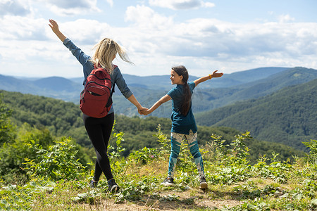母亲和孩子背着背包在山上享受。家庭旅行、冒险和旅游的概念。