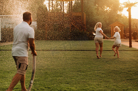 一个男人用软管把水倒在草坪上的妻子和女儿身上