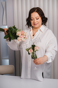 一位身穿白衬衫的成年女性站着，另一只手拿着洒有玫瑰的玻璃杯和一束玫瑰花。