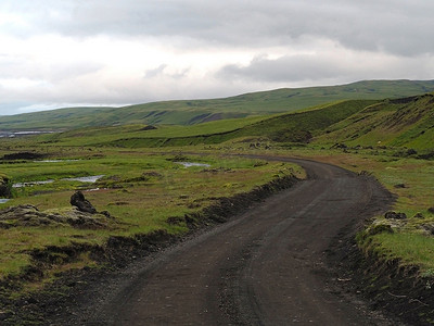 肮脏的山路穿过荒凉的风景，绿草如山，水坑通往冰岛内陆的山区