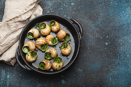 Escargots de Bourgogne 蜗牛配大蒜黄油和欧芹在黑色铸铁锅中，在质朴的石头背景顶视图上，传统的法国美食，文字空间。