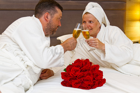 情侣躺在床上，用香槟碰杯，庆祝周年纪念，庆祝恋人的生日或浪漫约会