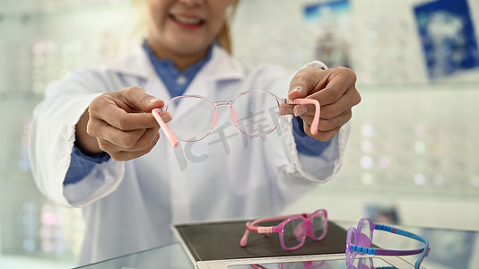 女配镜师站在眼镜店里拿着眼镜对着镜头微笑的照片