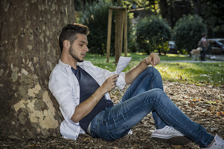 绿色阅读摄影照片_在公园放松的年轻人阅读纸页