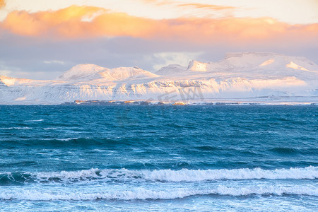 大海旅行摄影照片_日出蓬松的云彩和风雨如磐的大海与冰岛的雪山。