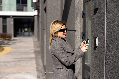 女性使用手机上的应用程序输入进入和通过建筑物的密码，女性按下控制面板上的按钮以解除智能家居系统