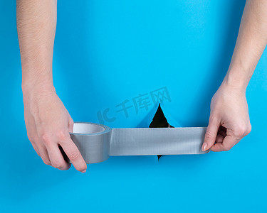 女人在蓝色背景上的一个洞上贴银胶带。