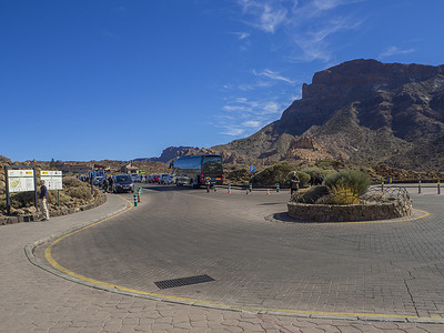 西班牙、加那利群岛、特内里费岛、泰德国家公园，2017 年 12 月 21 日，在 Roque Cinchado 著名的 pitoresque 岩层 Roques de Garcia 停车的交通圈与游客、公共汽车、停放的汽车、旅游告示和蓝天背景