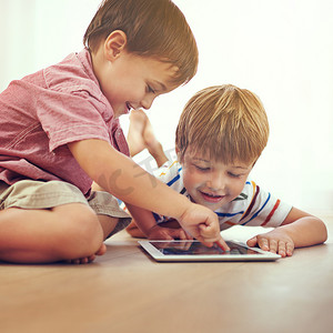 有了现代科技，做大哥变得更容易了……两个小男孩坐在地板上一起使用数字平板电脑。