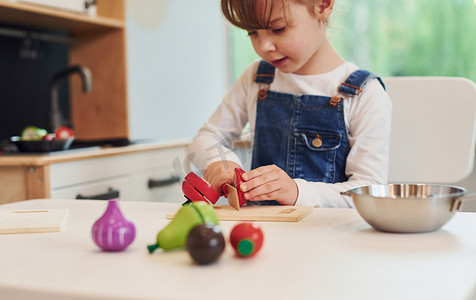 穿着休闲服的小女孩坐在桌边，在厨房玩玩具玩得开心