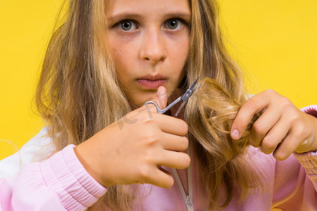 可爱的儿童美发师用黄色金属剪刀剪长长的金发