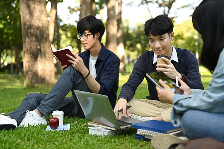 快乐的年轻多元化朋友坐在绿色的草坪上，准备上课。