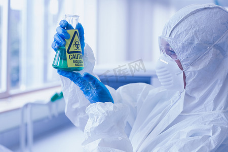 在实验室烧瓶中穿着防护服和危险化学品的科学家