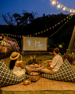 一对夫妇在带圣诞灯的热带花园里的户外电影院看电影