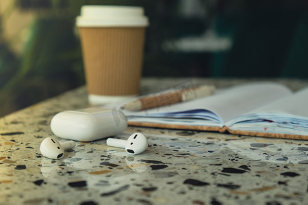 噪摄影照片_用带无线耳机的纸质笔记本带走工艺回收纸杯中的咖啡。