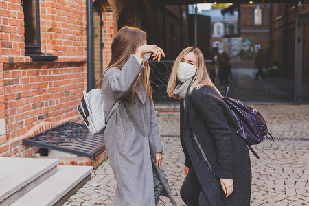 戴着医用口罩的年轻漂亮女孩朋友在城市的秋天晚上在户外玩得开心，笑着发疯 — 流行病概念的终结