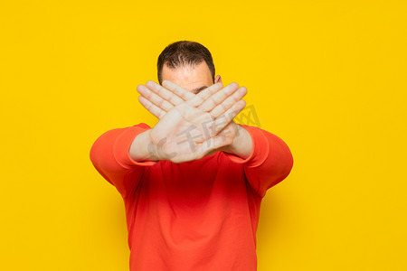 信号站摄影照片_西班牙裔男子站在黄色背景上，拒绝表达交叉双臂和手掌遮住脸，做出一个消极的信号。