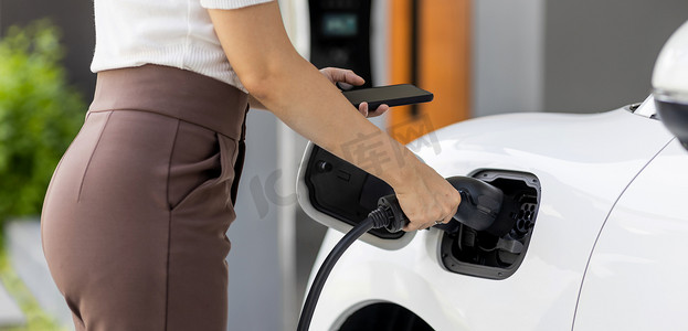 自动充电摄影照片_特写进步女性在家庭充电站为她的 EV 汽车充电。