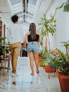 情侣旅行摄影照片_走在热带旅馆走廊的年轻夫妇。