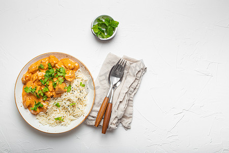 传统模板摄影照片_传统的印度菜咖喱鸡配印度香米和新鲜香菜，放在白色混凝土桌子背景的质朴白盘子上。