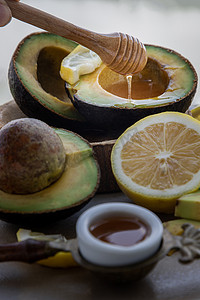 蜂蜜柠檬摄影照片_蜂蜜从木棒滴头滴入切成两半的新鲜有机鳄梨和蜂蜜柠檬片的特写镜头。
