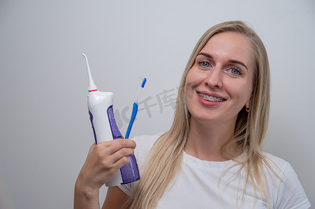 微笑的白种女人拿着冲洗器和牙刷，牙齿上戴着牙套。