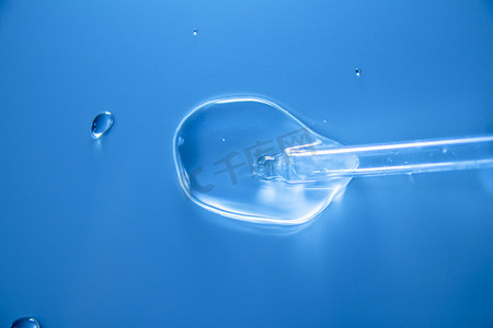 在实验室玻璃移液器的蓝色背景上，带有化妆品液滴的水泡。