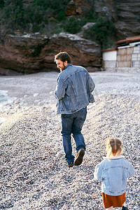 石子落下摄影照片_在落基山脉的背景下，小女孩在卵石滩上追着微笑的爸爸