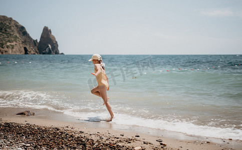 在阳光下奔跑摄影照片_可爱的小女孩在清澈湛蓝的大海的映衬下沿着海边奔跑，在夏日的阳光下欢欣鼓舞。
