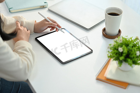 女性员工在办公桌空白空屏幕数字平板电脑上使用手写笔书写的裁剪图像