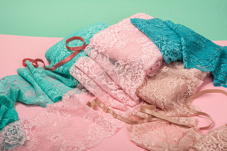 粉红色背景中用于内衣、内裤和胸罩的一堆颜色丰富的亮蕾丝