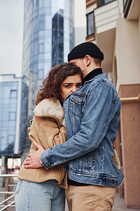 在商业大楼附近的城市里，一对穿着休闲保暖衣服的快乐夫妇在户外互相拥抱