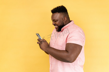 留着胡子的快乐男人使用手机的侧视图，表情愉快，沉迷于智能手机。