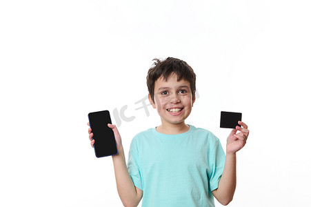 可爱的少年对着镜头开心地笑着，展示智能手机和一张黑色信用卡，上面有免费的促销文字空间