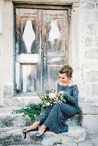 膝盖上放着一束鲜花的新娘坐在门附近一栋老建筑的台阶上