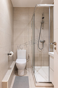 小浴室的入口，墙壁和地板上铺有米色大理石瓷砖，设有白色干净的卫生间、梳妆台和玻璃淋浴区。