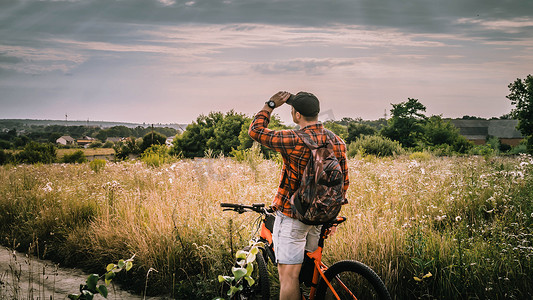 眺望远方人摄影照片_一个骑自行车的年轻人在大自然中，在田野里眺望远方，一个骑自行车的运动者。