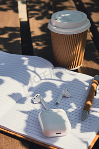 噪摄影照片_用带无线耳机的纸质笔记本带走工艺回收纸杯中的咖啡。