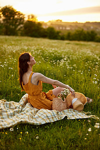 一位身穿橙色裙子的女士坐在洋甘菊花田里，手里拿着一顶草帽，享受着夕阳